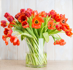 Red tulips in a vase on a wooden background
