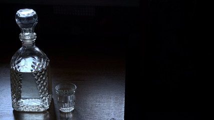 A bottle of vodka and a glass on a wooden table. Dark background