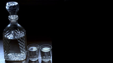 A bottle of vodka and two glasses on a wooden table. Dark background