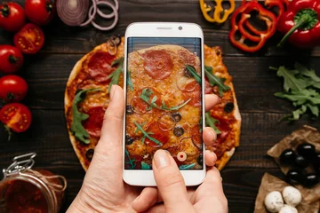 Foto auf Acrylglas Pizzeria Essen fotografieren. Hände fotografieren köstliche Pizza mit Smartphone