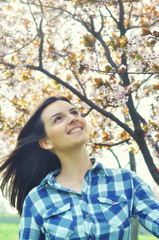 Outdoors portrait of beautiful girl standing between cherry tree in full bloom in spring.