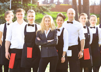 A large group of waiters and waitresses in the open air stand one after another