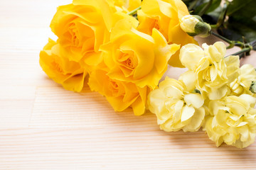 木のテーブルの上の黄色いバラとカーネーションの花