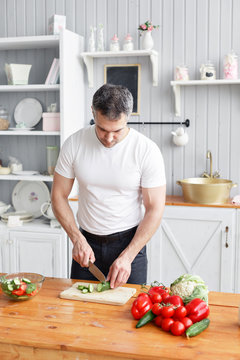 Middle-aged athlete, cuts vegetables salad of cucumber and tomato. Vegetarian food