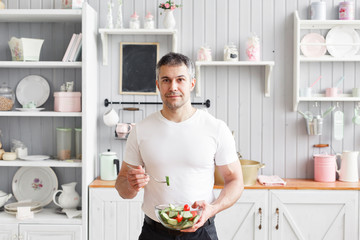 Middle-aged athlete, holding a bowl of a plate with a prepared salad of cucumber and tomato. Vegetarian food