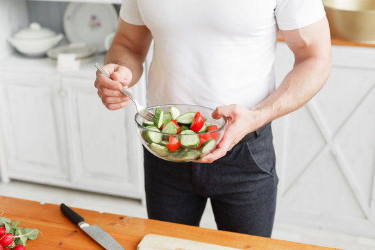 Middle-aged athlete, holding a bowl of a plate with a prepared salad of cucumber and tomato. Vegetarian food
