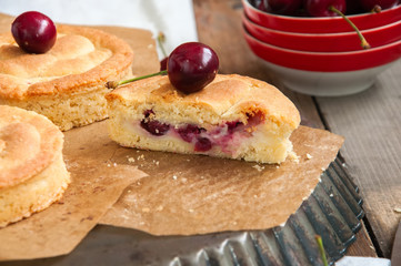 Whole and slice of cherry custard pie served on a vintage baking form on a wooden background.
