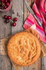 Whole and slice of cherry custard pie served on a vintage baking form on a wooden background.