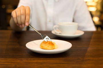 Hand holding a fork eating Eclair with coffee cup