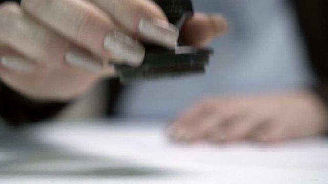 Девушка ставит печать на документ. Крупный план.