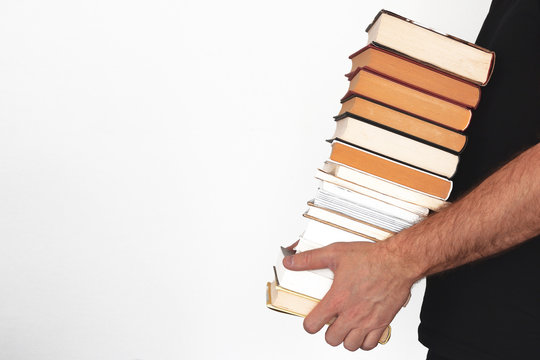 Young man holding a pile of books against a white wall. Empty copy space for Editor's text.