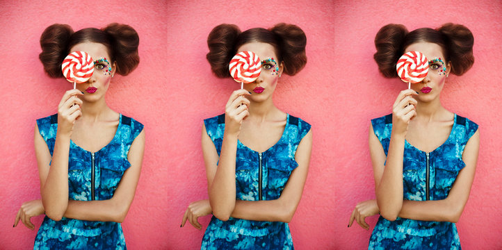 Studio closeup colorful portrait of young sexy fashion girl posing on pink wall background in summer style outfit with pink lollipop wearing blue dress. Creative image of pretty girl with lollipop.