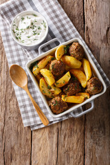 Baked meat balls with potato wedges and sour cream sauce close-up on the table. vertical top view