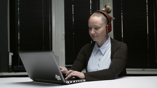 Девушка в наушниках работает в офисе за компьютером.