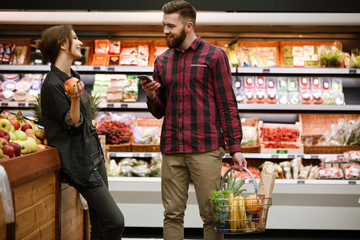 Smiling young loving couple talking in supermarket