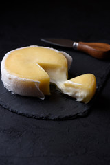 Butter soft creamy sheep cheese from Seia region Portugal on black slate board, with one piece cut and cheese melting