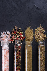 Assorted ground spices in bottles on dark stone background with copy-space. Himalayan pink salt, herbs de provence, peppers and grill mix.