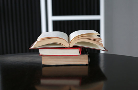 Open book with stack of hardcover books on wooden table.