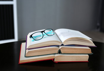 Open stack hardback books with glasses on wooden table. Education background.