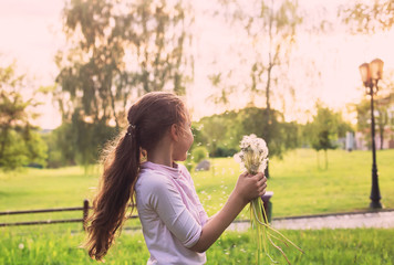  Beautiful child with dandelion flower in sunny spring park. Happy kid having fun outdoors at sunset.