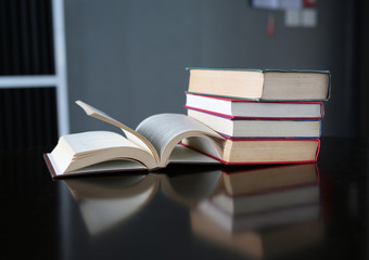 Open book and stack of hardcover books on wooden table.
