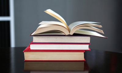 Open book with stack of hardcover books on wooden table.