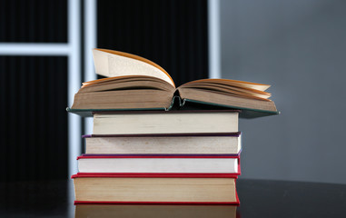 Open book with stack of hardcover books on wooden table.