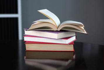 Open book with stack of hardcover books on wooden table.