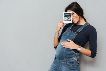 Pregnant smiling woman showing ultrasound scans