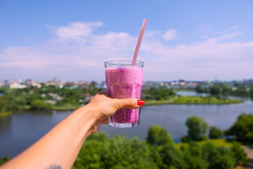 Woman holding  glass,  of smoothie close-up, outdoors. Beautiful view