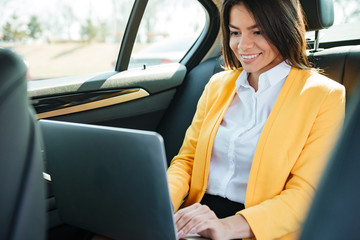 Businesswoman sitting on back seat of car and working