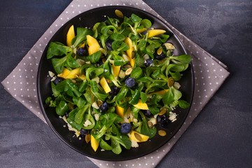 Mango, blueberries and cheese salad on black plate. View from above, top studio shot