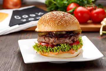 Big tasty burger on a white plate over wooden background.