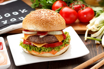 Big tasty burger on a white plate over wooden background.