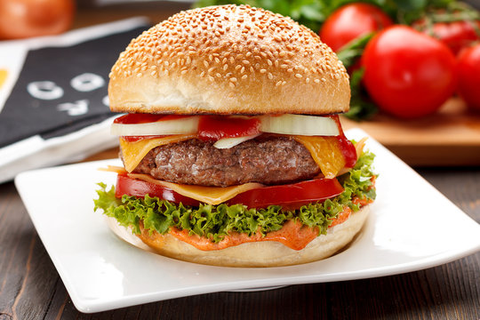 Big tasty burger on a white plate over wooden background.