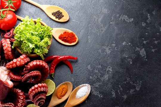 Freshly prepared octopus with vegetables and spices in wooden spoones over dark stone background