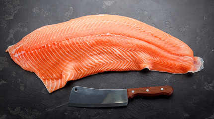 Fresh raw salmon fillet with chef knife over dark stone background