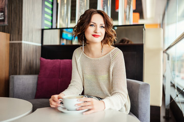 Portrait of young gorgeous female drinking tea and thoughtfully looking out of the coffee shop window while enjoying her leisure time alone, nice business woman lunch in cafe during her work break