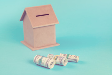 The concept of financial savings to buy a house. Money box, dollars in rolls, isolated on blue background. Toned.