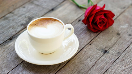 Hot coffee and red rose on a wooden table.