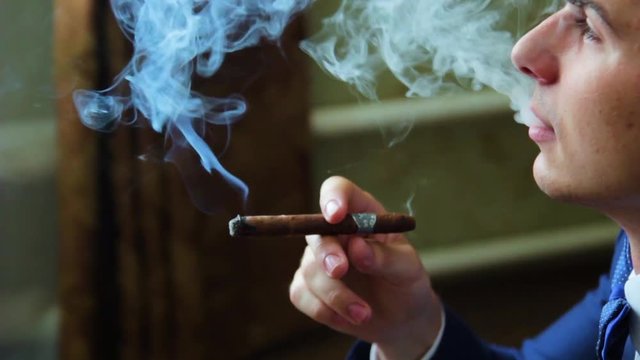 the man with the cigar blows smoke