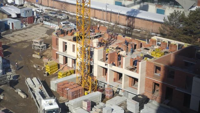 There is a construction of a new house, builders lay bricks, using a crane and heavy equipment. 4k