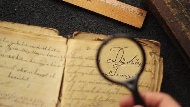 Hands searching in a vintage manuscript with magnifying glass.