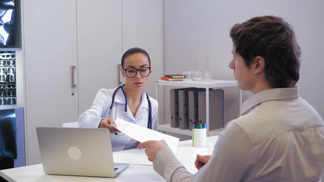 Doctor giving patient prescription on medicine. Mixed race woman wearing in white coat. Man holding px and listen instruction.