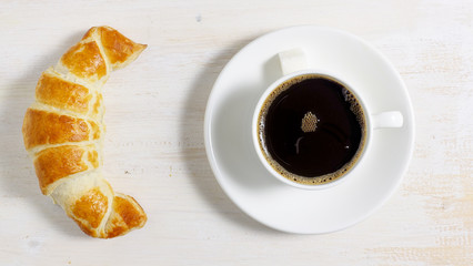Homemade croissant with natural coffee in a cup and saucer on the table