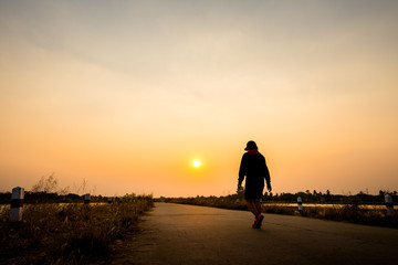 Fototapeta na wymiar silhouette woman walking on road at sunset background