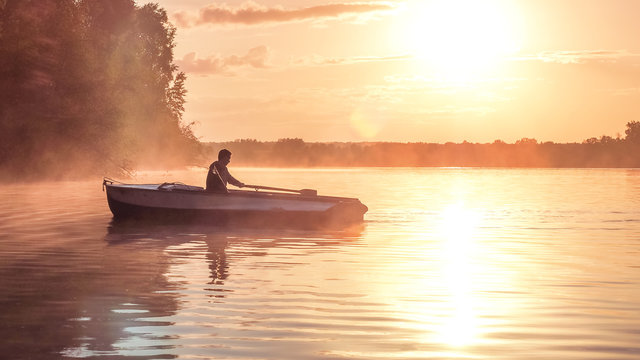 A young guy rides a boat on a lake during a golden sunset. Image of silhouette, Rower at sunset. Man rowing a boat in backlight of the sun