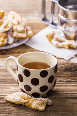 A cup of hot tea, fresh faworki on a wooden table