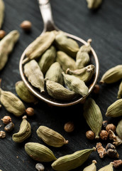 Metal spoon with cardamon dry seeds in it on a black wooden table, vertical