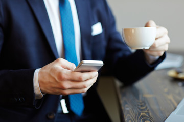 Closeup portrait of unrecognizable elegant businessman working in cafe, drinking coffee and browsing internet via smartphone during break
